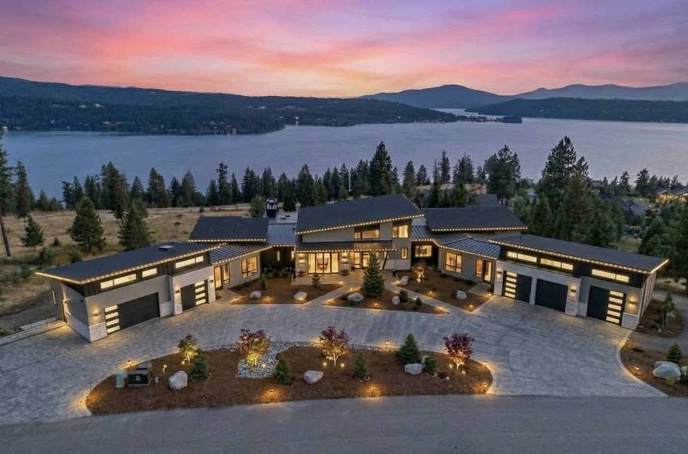 Aerial view of a modern lakeside home at sunset, every roofline outlined in warm white lights