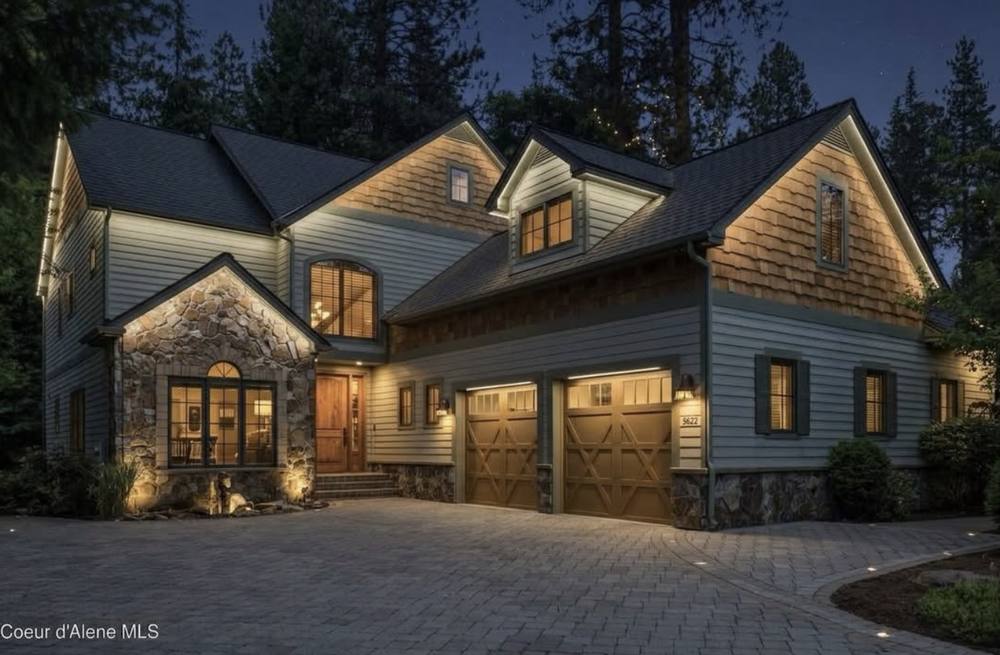 Two-story home with cedar shingles and soft lighting along the eaves and gables